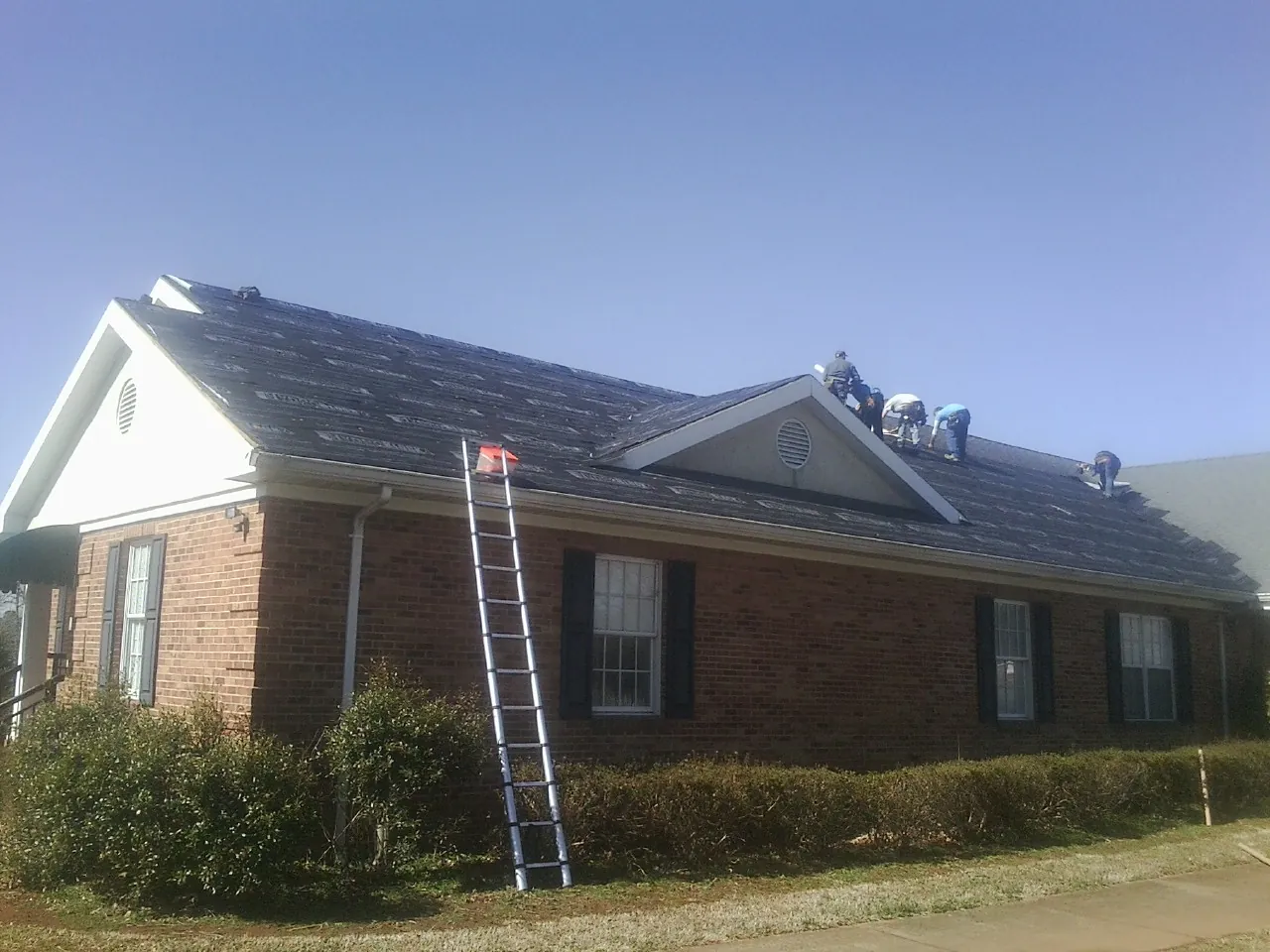 Crew tearing shingles off a brick ranch roof with a ladder set — Emergency Roof Repair work by our crew in Vernalis