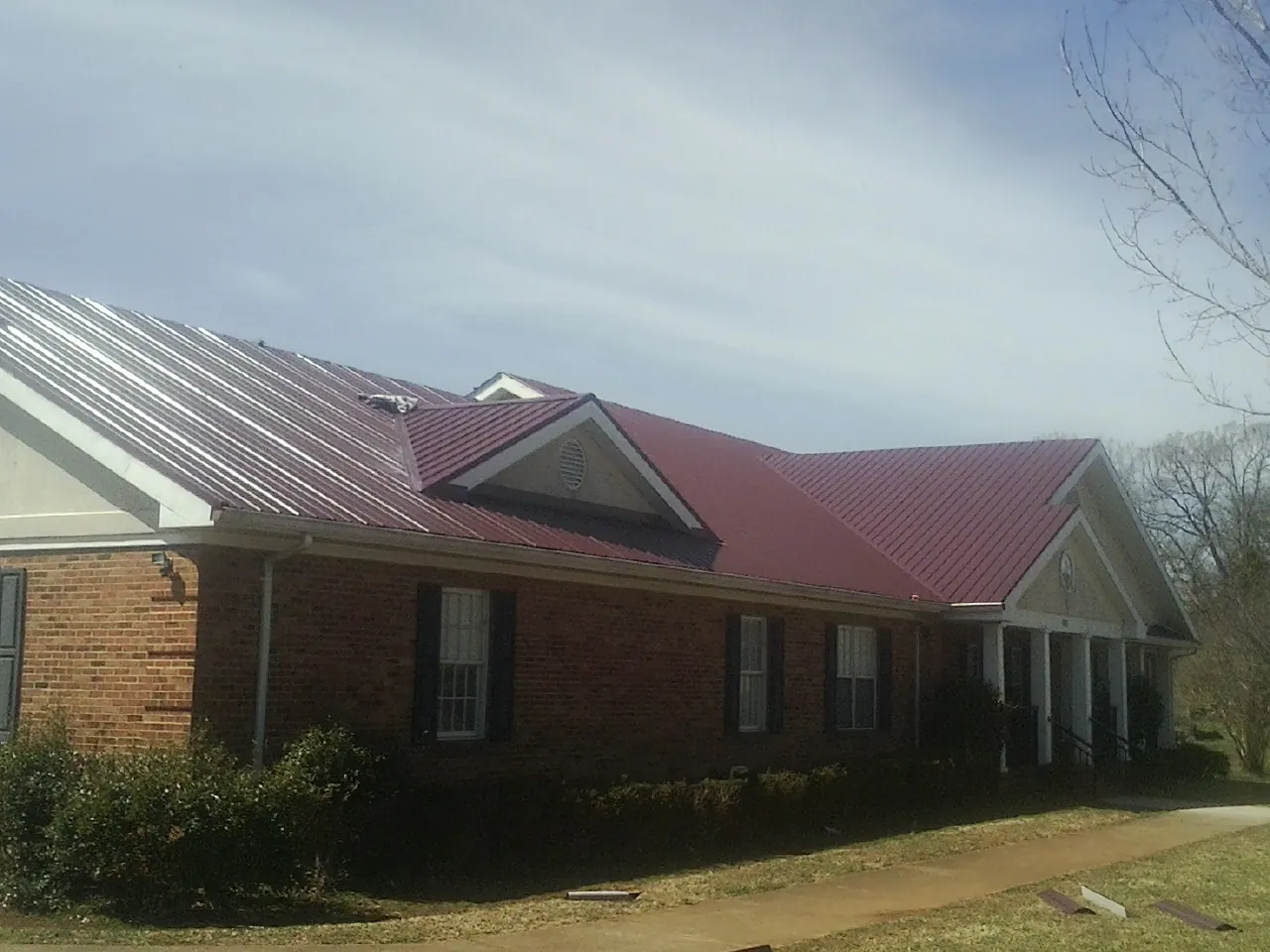 Red metal roof with gabled entries on a long brick building, from a Hail Damage Roof Repair job in Vernalis
