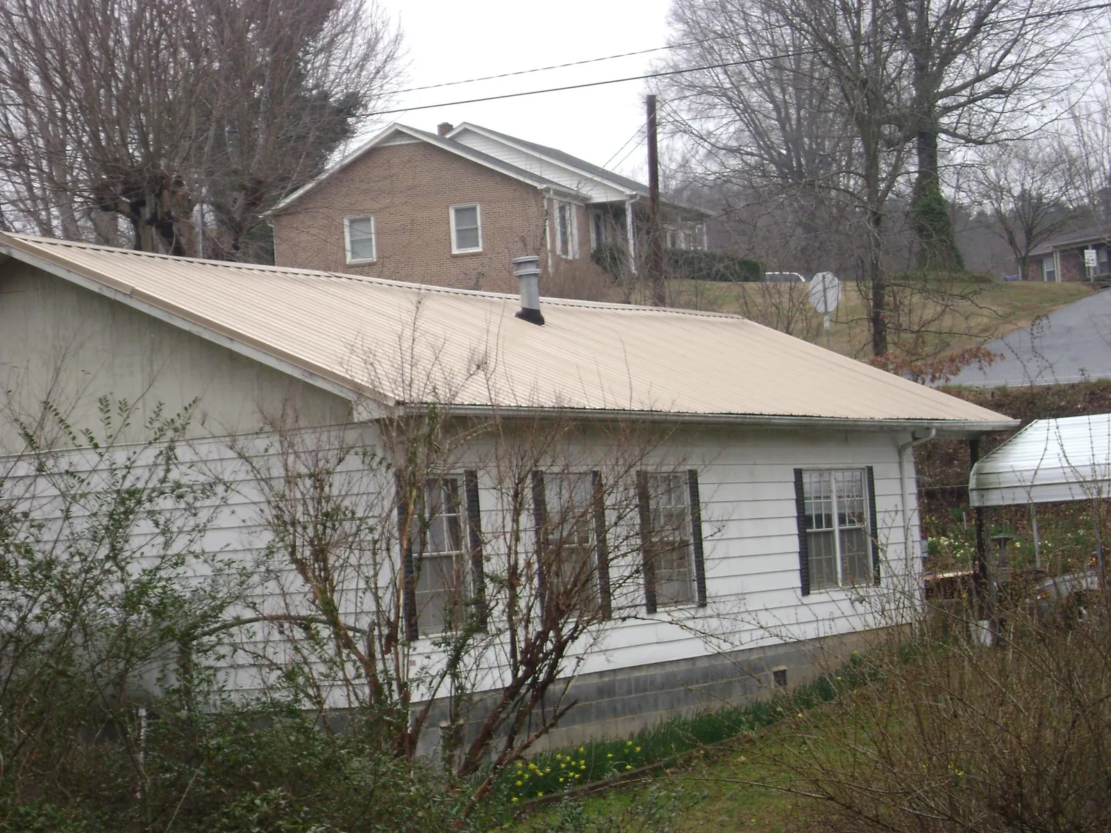 Tan metal roof on a white sided house set into a hillside — Commercial Roofing by Roofing Brothers in Vernalis
